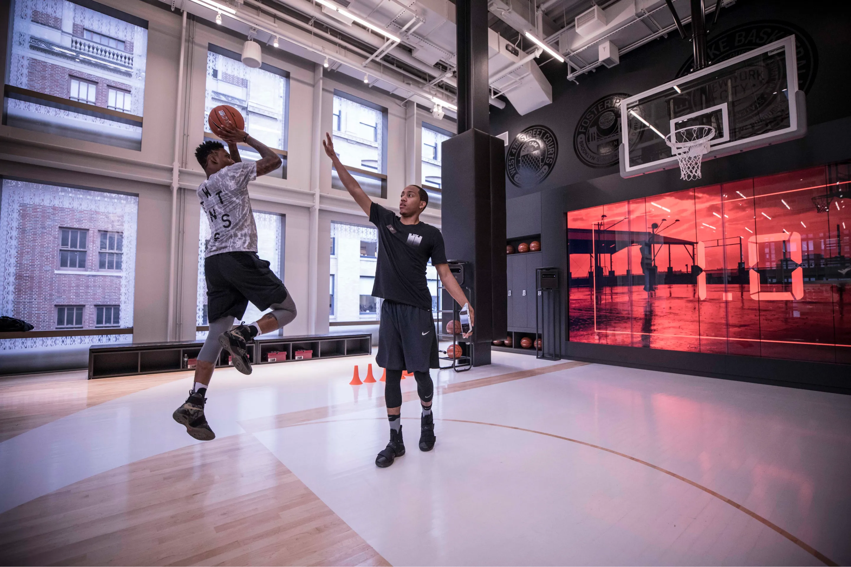 Two athletes playing basketball on the court in the Trial Zone Experience at the Nike Soho Store in front of the wall-sized screen